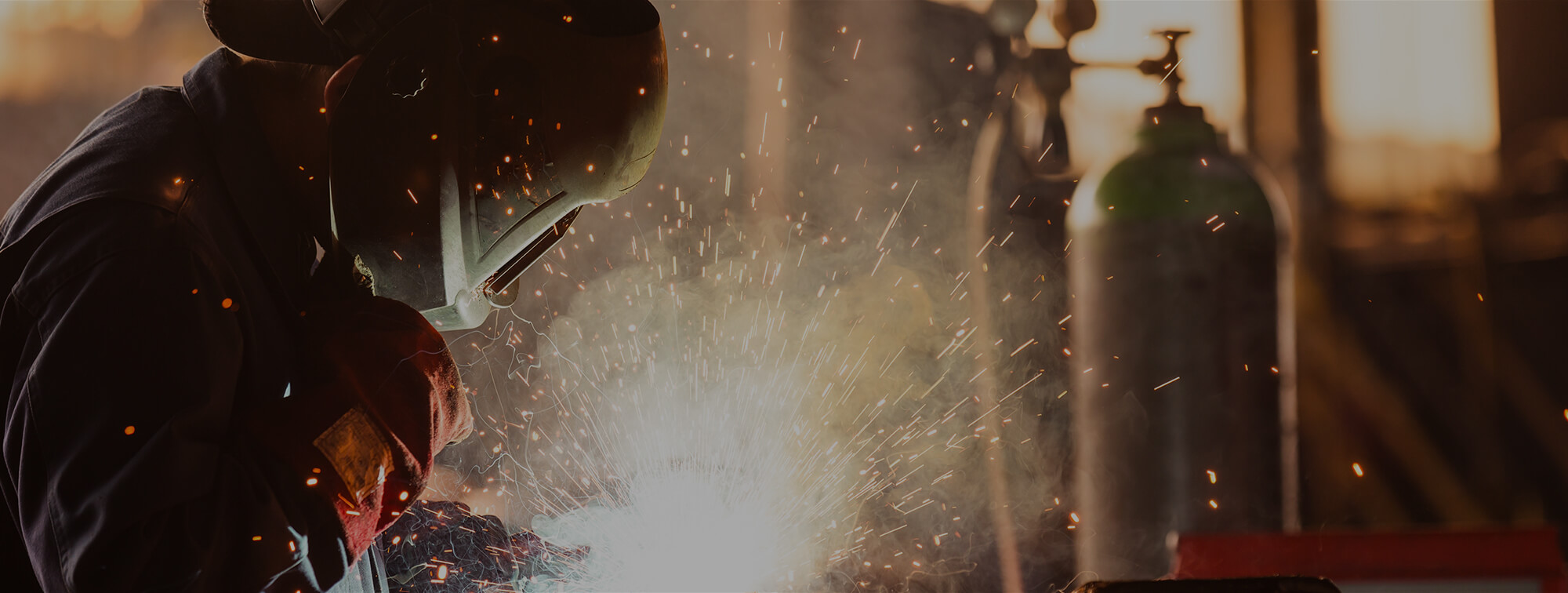 Shop technician welding with a welders mask and flying sparks